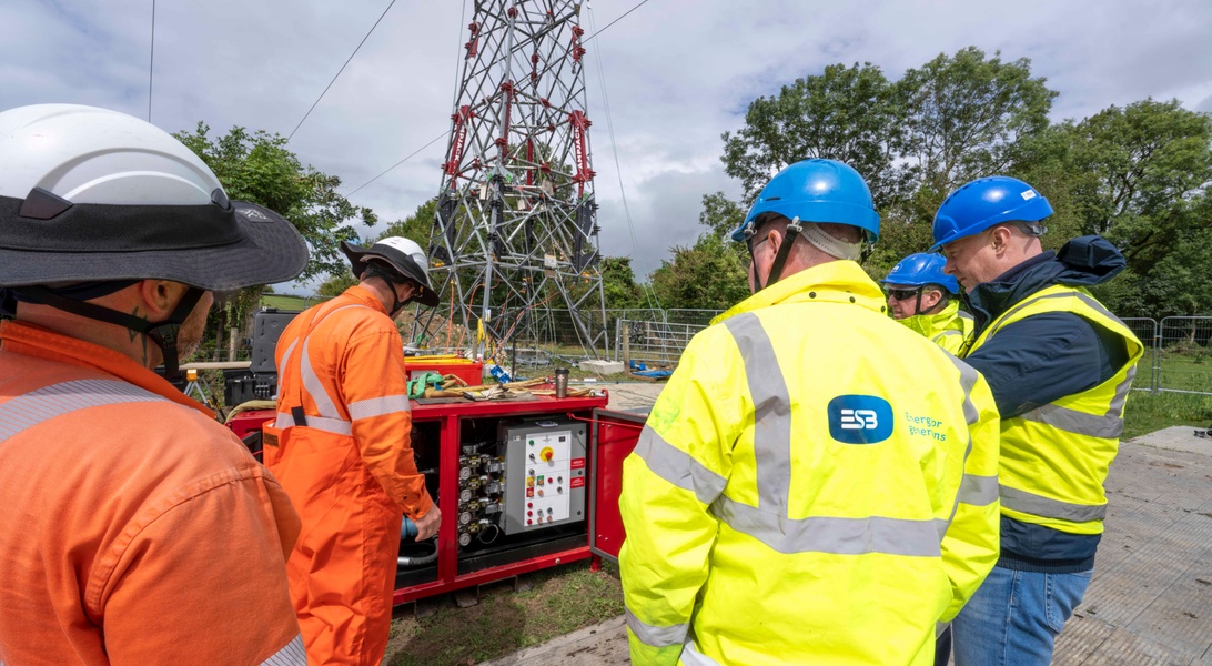 Personnel observing tower-raising technology being used during an electricity network upgrade.